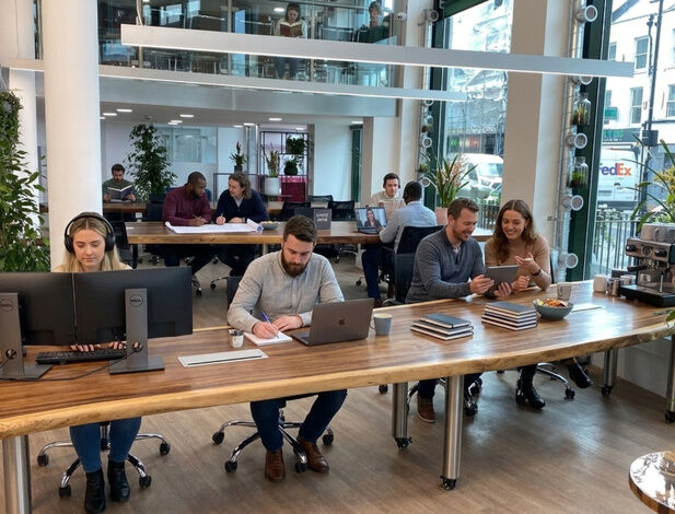 Members at shared coworking desks under a glazed roof at Camden Gateway