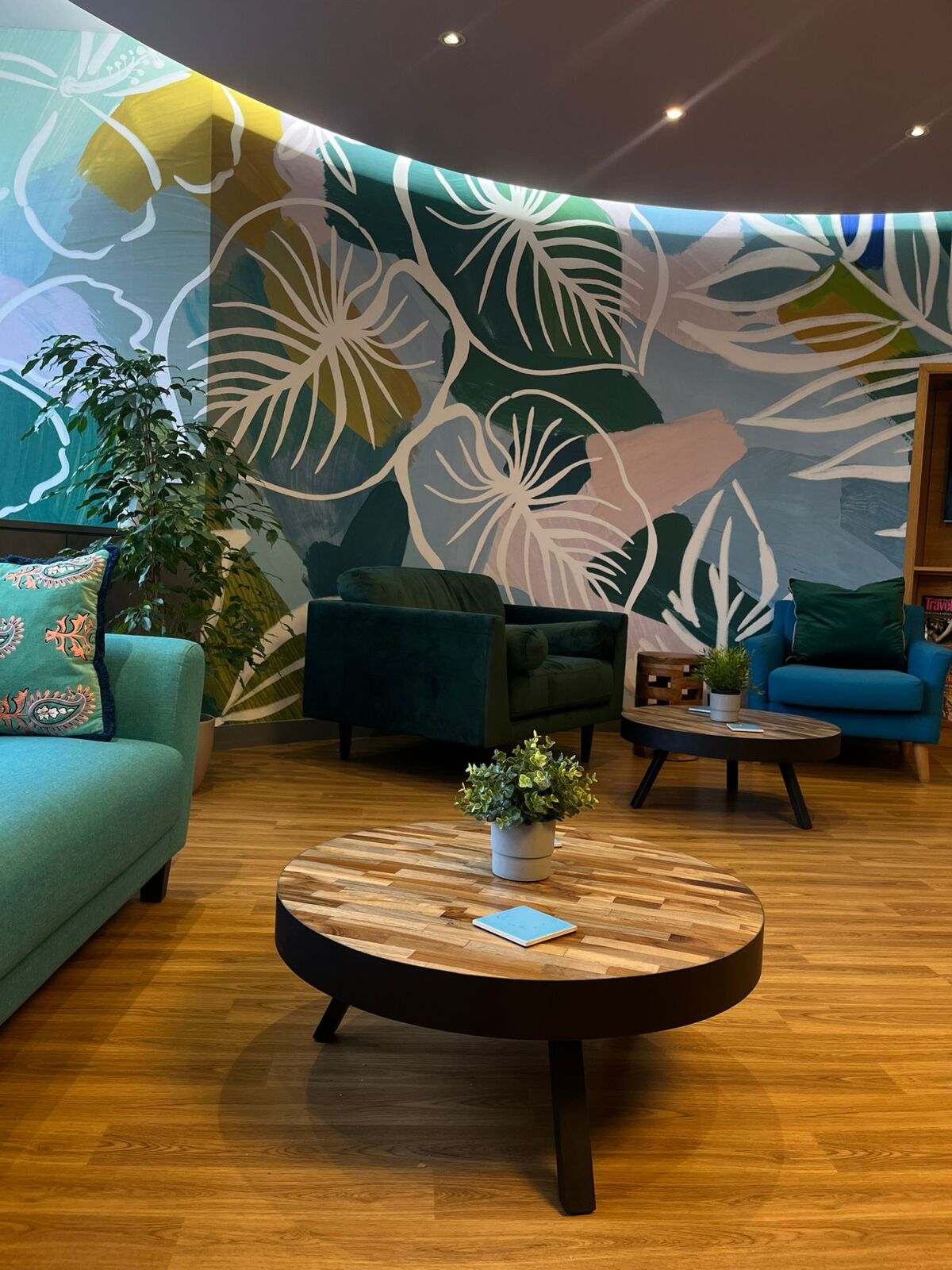 Teal armchairs and a coffee table in the TBXH lounge with leaf-print wallpaper