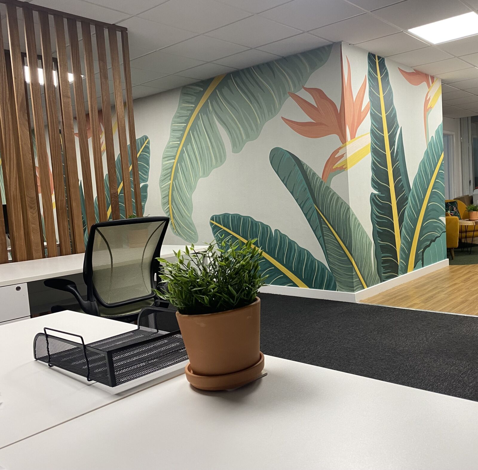 Desk with a desk tidy and plant in front of a tropical mural at TBXH
