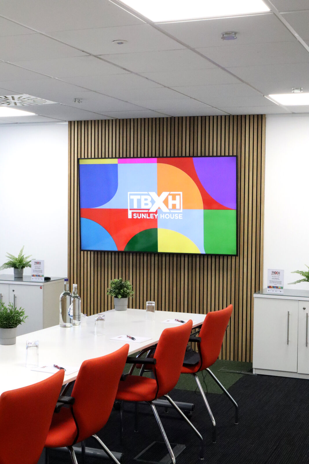 Meeting room at TBXH with a white table, red chairs and a wall screen